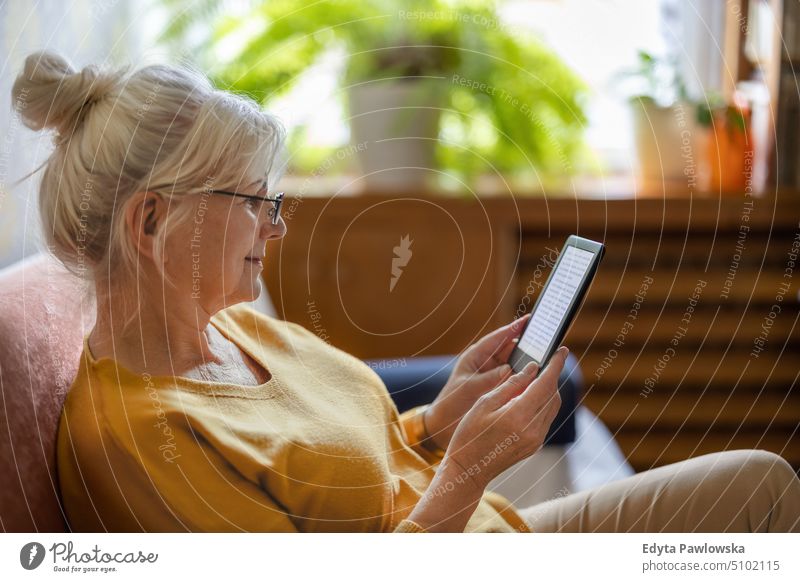 Ältere Frau benutzt einen E-Reader und liest ein E-Book zu Hause Lächeln Glück genießend positiv Freude Menschen Senior reif älter heimwärts alt Alterung