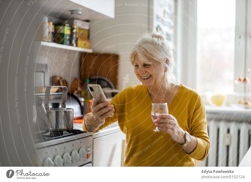 Ältere Frau benutzt Mobiltelefon zu Hause Lächeln Glück genießend positiv Freude Menschen Senior reif älter heimwärts alt Alterung häusliches Leben Großmutter