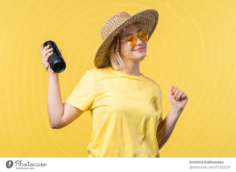 Eine Frau tanzt, genießt auf gelbem Studiohintergrund. Sie bewegt sich zum Rhythmus der Musik. Junge Frau hört Musik durch drahtlose tragbare Lautsprecher - modernes Soundsystem.