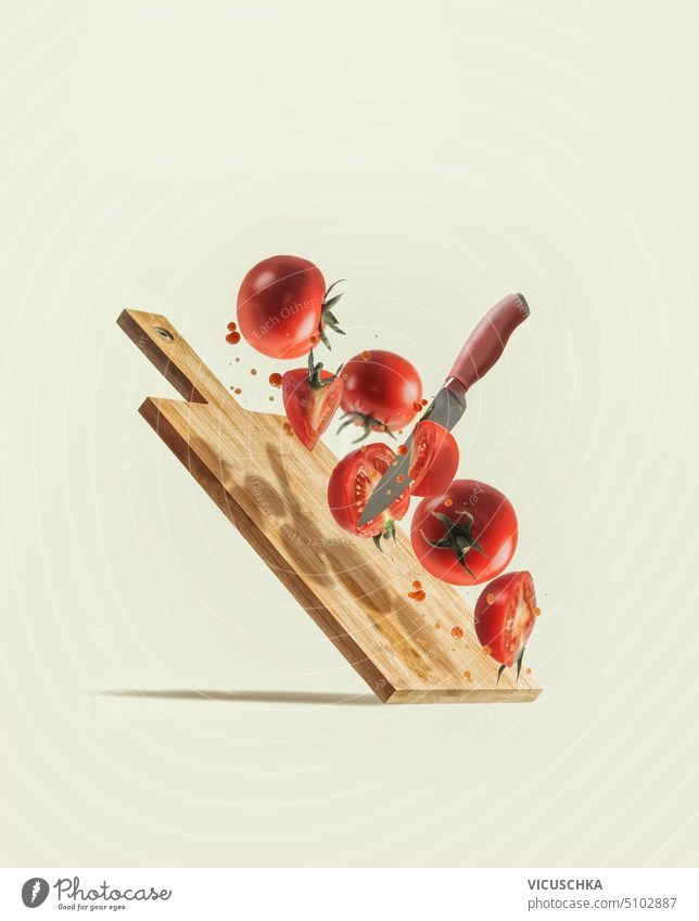 Fliegende geschnittene Tomaten, Messer und Holzschneidebrett auf blassbeigem Hintergrund. Schwebende Zutaten mit frischem Gemüse. Kreatives Lebensmittelkonzept. Vorderansicht.