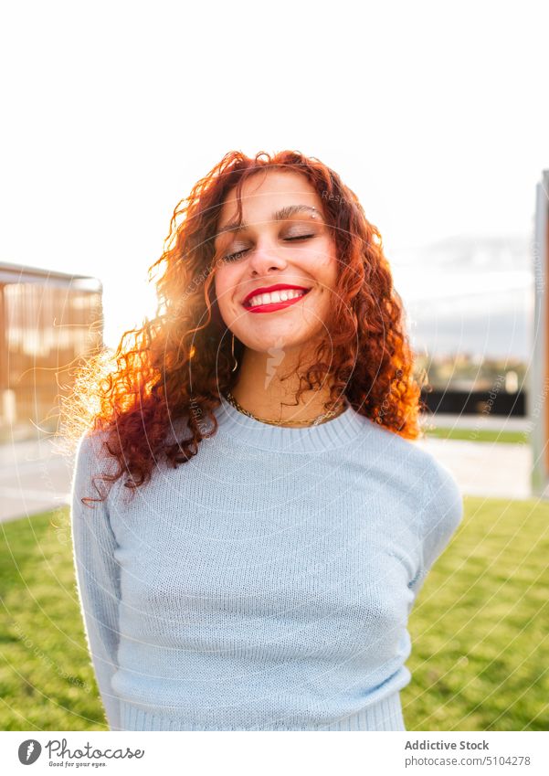 Glückliche junge Frau in der Nähe von Rasen Lächeln Sonnenaufgang Straße krause Haare rote Haare Morgen früh Pullover heiter Rotschopf lässig positiv Sommer