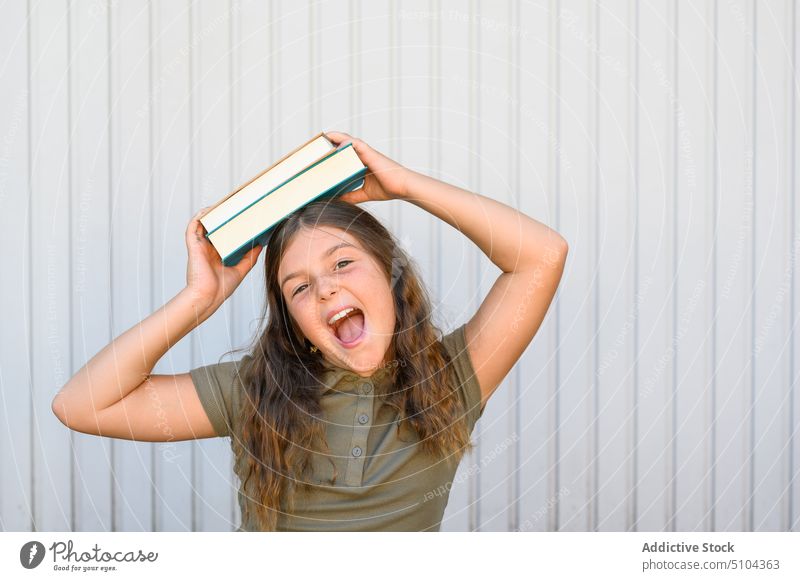 Fröhliche Schülerin mit Büchern, die gegen die Wand schreien Mädchen Buch Wissen aufgeregt Porträt Glück heiter Bildung sorgenfrei Mund geöffnet Schulmädchen