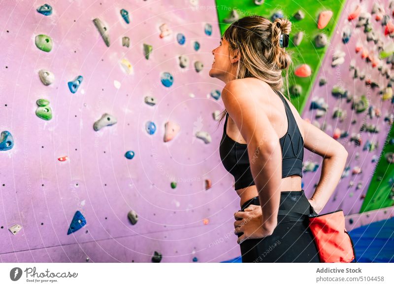 Sportlerin schaut auf Kletterwand Aufsteiger Lächeln Wand bereit Fitnessstudio Training froh Unterlage Mut Frau Freude Hand auf der Taille Bouldern Glück Tasche
