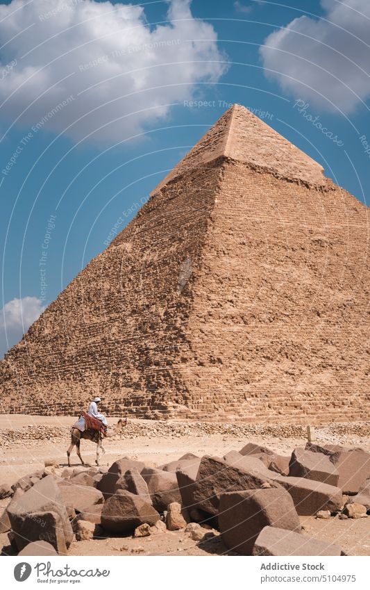 Anonymer einheimischer Mann reitet auf einem Kamel in der Nähe einer antiken Pyramide in der Wüste Pyramiden wüst Beduinen Camel Architektur Mitfahrgelegenheit
