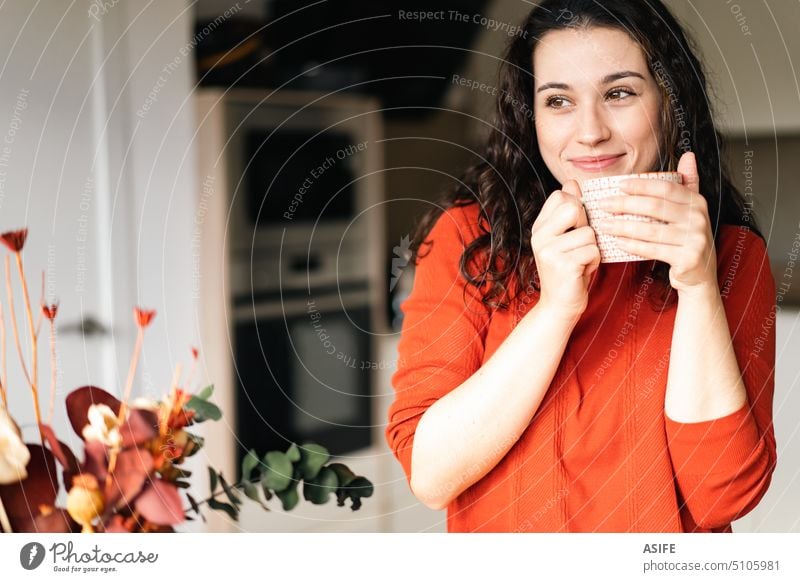 Junge glückliche Frau, die ein heißes Getränk in der Küche genießt Kaffee Tasse Tee trinken Stehen Wegsehen verträumt heimwärts Lifestyle Beteiligung Glück