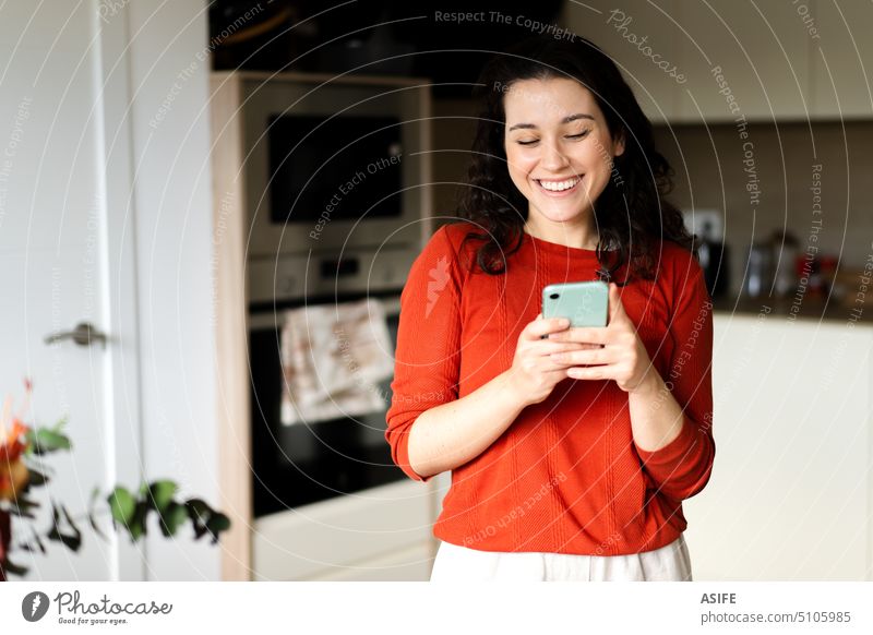 Junge glückliche Frau benutzt ihr Telefon in der Küche heimwärts Glück Lächeln Smartphone Mobile Lachen jung sprechend attraktiv Mitteilung Internet