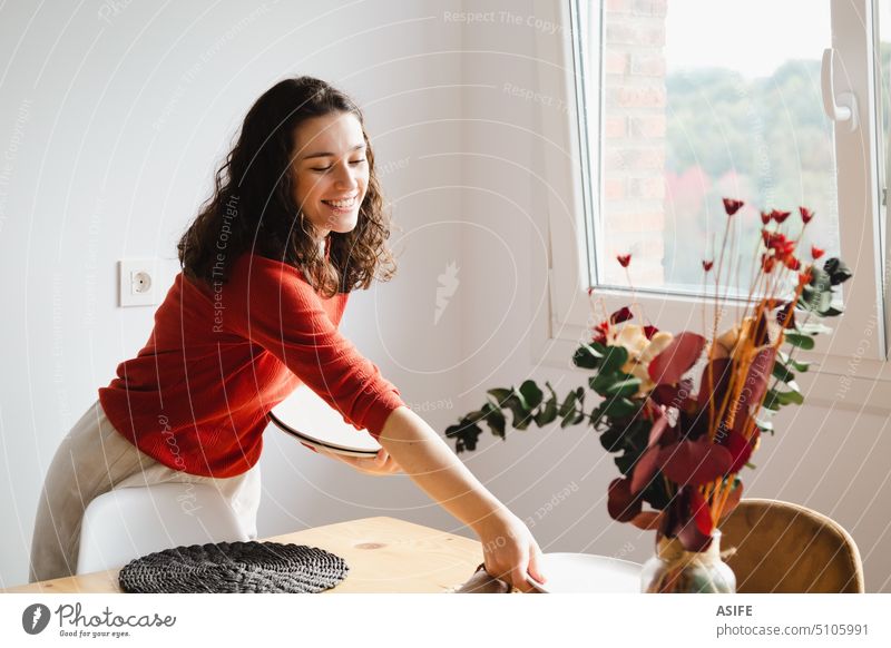 Junge glückliche Frau deckt den Tisch zu Hause Einstellung Ort dekorierend Blumen Geschirr heimwärts speisend Speise hölzern Trockenblumen Eukalyptus Dekor Vase