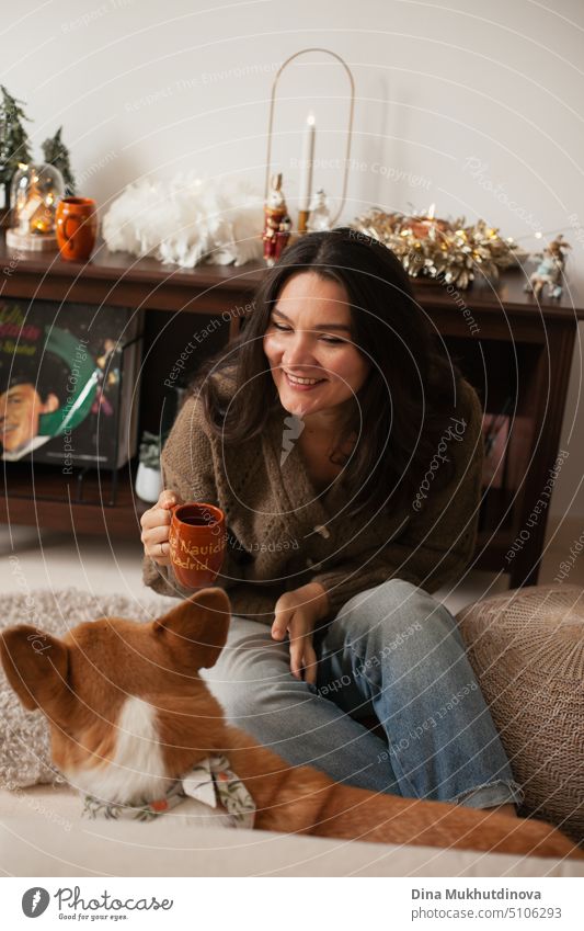 Erwachsene brunette kaukasische Frau spielt mit Corgi Hund und trinken Kaffee zu Hause Wohnung für Weihnachten Urlaub Saison dekoriert. heimwärts schön Glück