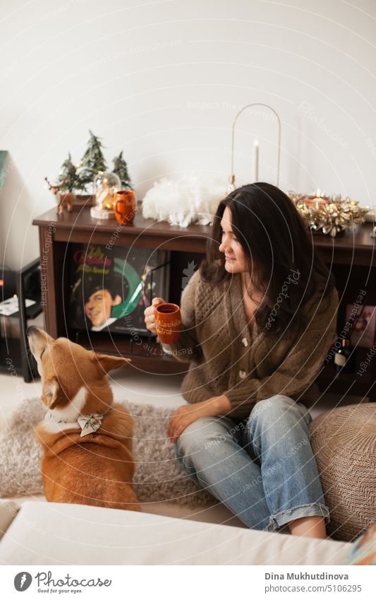 Erwachsene brunette kaukasische Frau spielt mit Corgi Hund und trinken Kaffee zu Hause Wohnung für Weihnachten Urlaub Saison dekoriert. heimwärts schön Glück