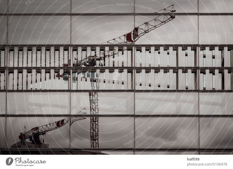 Kräne auf einer Baustelle spiegeln sich in einer Glasfassade einer modernen Architektur Kran Fassade Glasscheibe urban Ordnung Arbeitsplatz baugewerbe