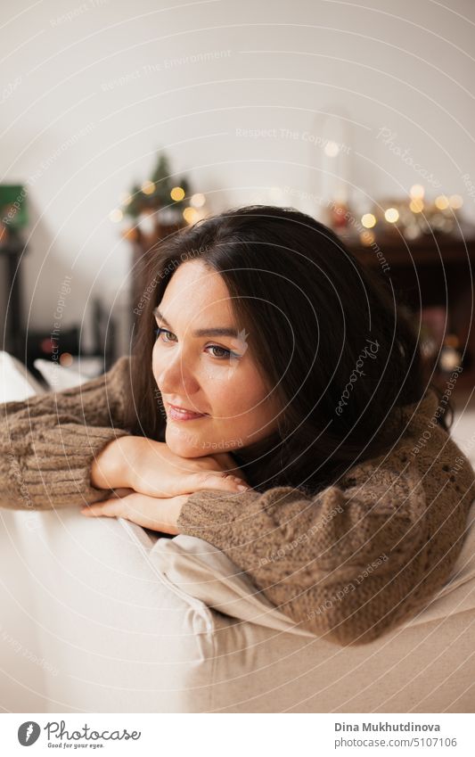 Schöne kaukasische Frau lächelnd in ihrem gemütlichen Haus Wohnung lehnt sich über die Couch. Closeup lässigen Lebensstil weiblichen Porträt. Millennial Leben. Expat-Leben. Erstellen komfortablen Raum um Sie herum.