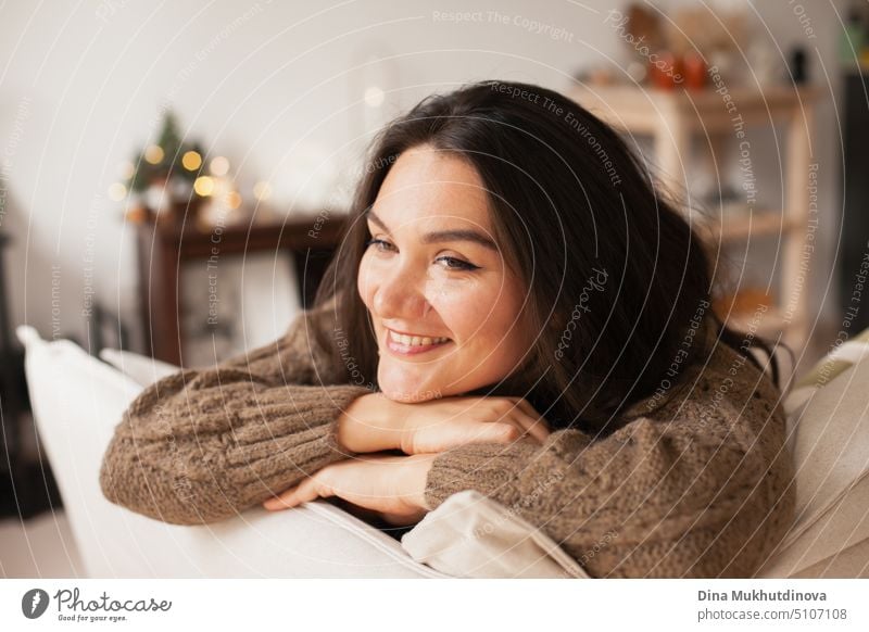 Schöne kaukasische Frau lächelnd in ihrem gemütlichen Haus Wohnung lehnt sich über die Couch. Closeup lässigen Lebensstil weiblichen Porträt. Millennial Leben. Expat-Leben. Erstellen komfortablen Raum um Sie herum.