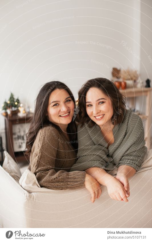 Zwei Frauen sitzen auf einer Couch in einer gemütlichen Wohnung. Familie verbringt Zeit zu Hause. Porträt von Schwestern lächelnd in modernen minimalen Interieur.