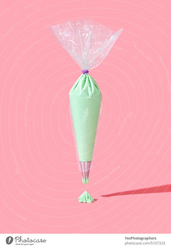 Zuckergussbeutel isoliert auf einem rosa Hintergrund. Grüne Buttercreme Glasur in einer Plastiktüte abstrakt Tasche backen Transparente hell Bonbon Feier