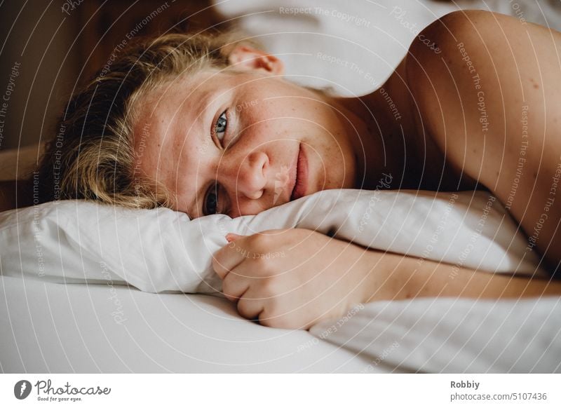 junge blonde Frau schaut im Bett liegend in die Kamera schlafen schlafen legen elegant verführerisch Frauenkörper Frausein Körperbewusstsein Schönheit