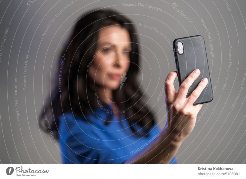 Lächelnde glückliche erwachsene Frau, die ein Selfie mit ihrem Smartphone auf grauem Hintergrund macht. Technologie, mobiles Gerät, soziale Netzwerke Konzept