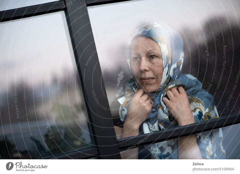 Lächelnde Frau mittleren Alters mit Schal auf dem Kopf, die durch schmutziges Fensterglas schaut reif älter Aussehen hinten dreckig Glas Gesicht Ausdruck Hände