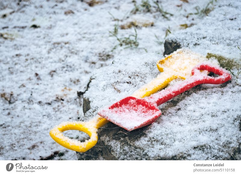 Zwei vergessene Kinderschaufeln unterm Schnee Spielplatz Schaufel Sandschaufel frischer Schnee Neuschnee kalt Winter rot verloren gelb Wetter Schneedecke weiß