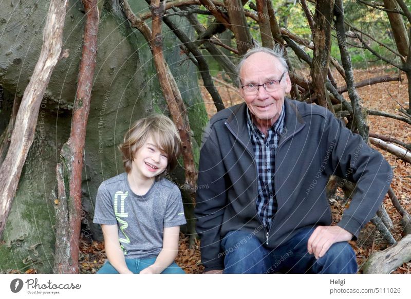 Opa und Enkel sitzen fröhlich im Wald in einem Tipi aus Ästen Mensch Kind Schulkind Junge Mann Senior Großvater freundlich Freude Spaß draußen Natur alt
