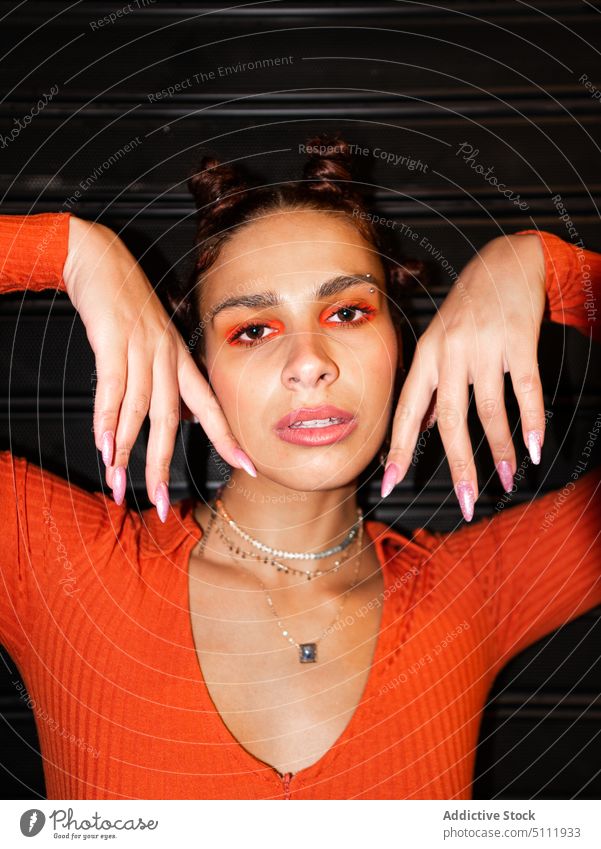 Stilvolle Frau berührt Gesicht und schaut in die Kamera ernst trendy Mund geöffnet Make-up Lidschatten orange Accessoire Porträt Bantuknoten Mode Vorschein