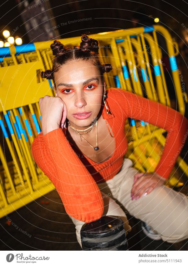 Stilvolle Frau sitzt nachts auf der Straße selbstbewusst Streetstyle lebhaft Make-up Mode orange Nacht Farbe Vorschein cool trendy hell ernst Voute Outfit jung