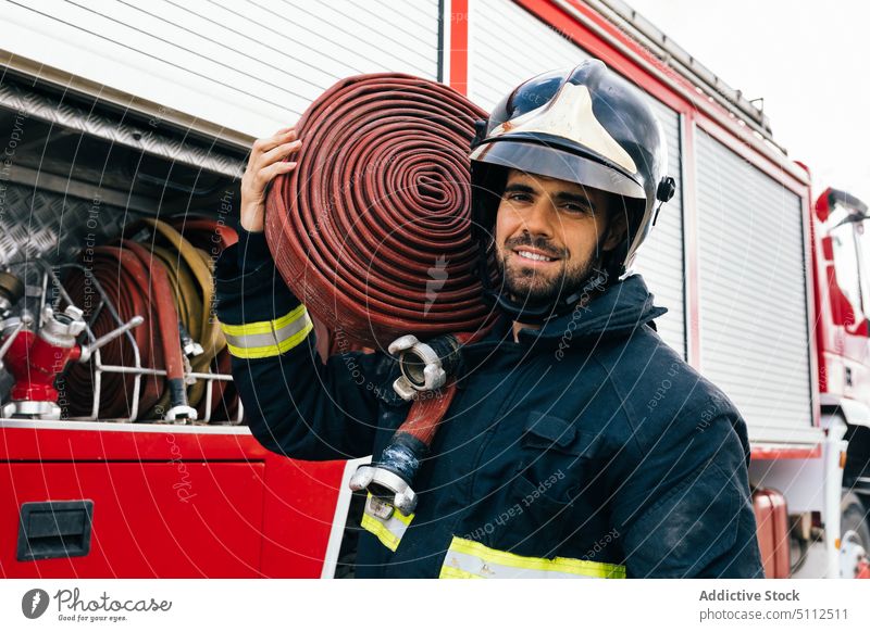 Hispanischer Feuerwehrmann mit Helm trägt Schlauch auf der Schulter Lächeln führen Feuerwehrauto Arbeit Uniform Porträt männlich Erwachsener hispanisch ethnisch