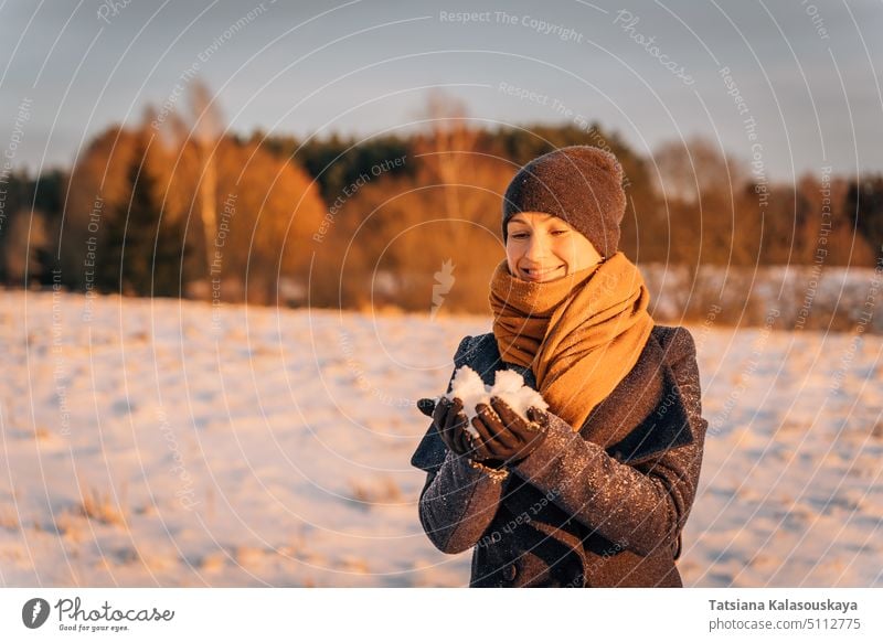 Lächelnde Frau mit Schal und Mütze hält eine Handvoll Schnee im Winter Hut Halt warme Kleidung Menschen Person Europäer weiß Erwachsener mittlerer Erwachsener