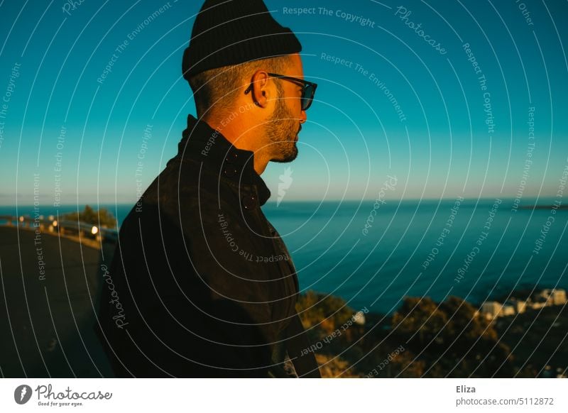 Mann mit Sonnenbrille und Mütze betrachtet das Meer von einem Aussichtspunkt Mensch blau seitlich Seitenansicht nachdenklich Erwachsen Hipster blauer Himmel