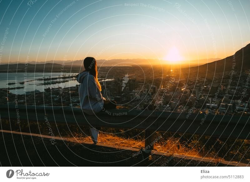 Frau sitzt auf einer Leitplanke und betrachtet den Sonnenaufgang über Kapstadt morgens Ausflug Sonnenlicht Mensch Freiheit Berge stimmungsvoll Reisen einsam