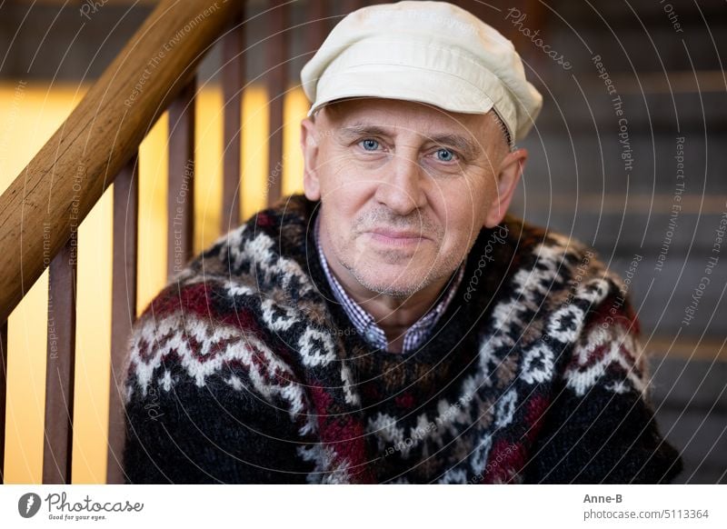 Portrait eines freundlichen zufrieden aussehenden Mannes, der mit Mütze und Strickpullover in einem Treppenhaus sitzt maskulin Erwachsene 1 Mensch 45-60 Jahre