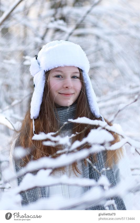Porträt eines langhaarigen Teenager Mädchens mit russischer Uschanka-Mütze im verschneiten Park Mädchenportrait Junge Frau mädchenhaft Winter mützenmädchen