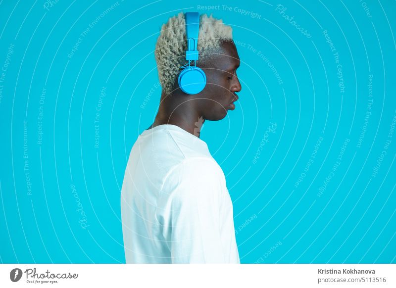 Gutaussehender schwarzer Mann mit trendiger Frisur und Kopfhörern im Studio vor blauem Hintergrund. Musik, Tanz, Radio-Konzept. Person hören schön Erwachsener