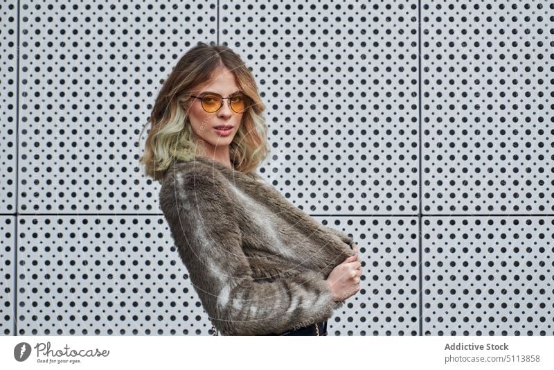Selbstsichere junge Frau mit Sonnenbrille und Blick in die Kamera Stil selbstbewusst Individualität Porträt Straße selbstsicher gewelltes Haar blond Pelzimitat