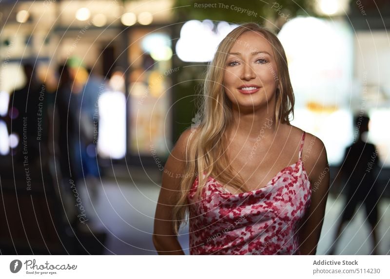 Fröhliche junge Frau schaut auf der Straße in die Kamera Lächeln Nacht Glück urban Porträt Stil Nachtleben Abend heiter blond positiv froh Kleid Optimist dunkel