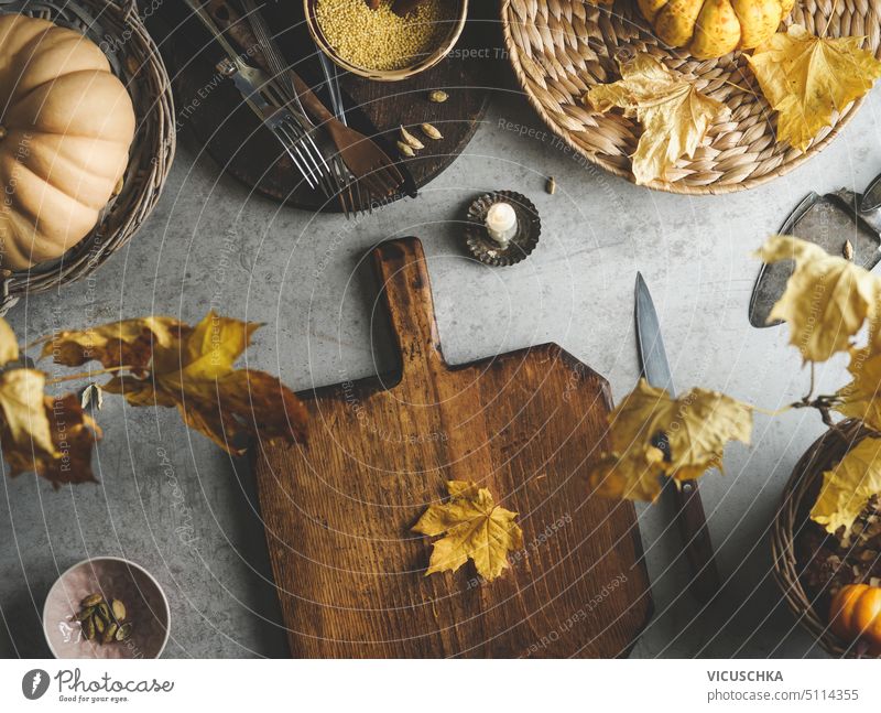Herbst Kochen Hintergrund mit Holzschneidebrett, gelbe Herbstblätter, Messer und Kürbis auf Beton Küchentisch. Saisonales Kochen zu Hause. Ansicht von oben.