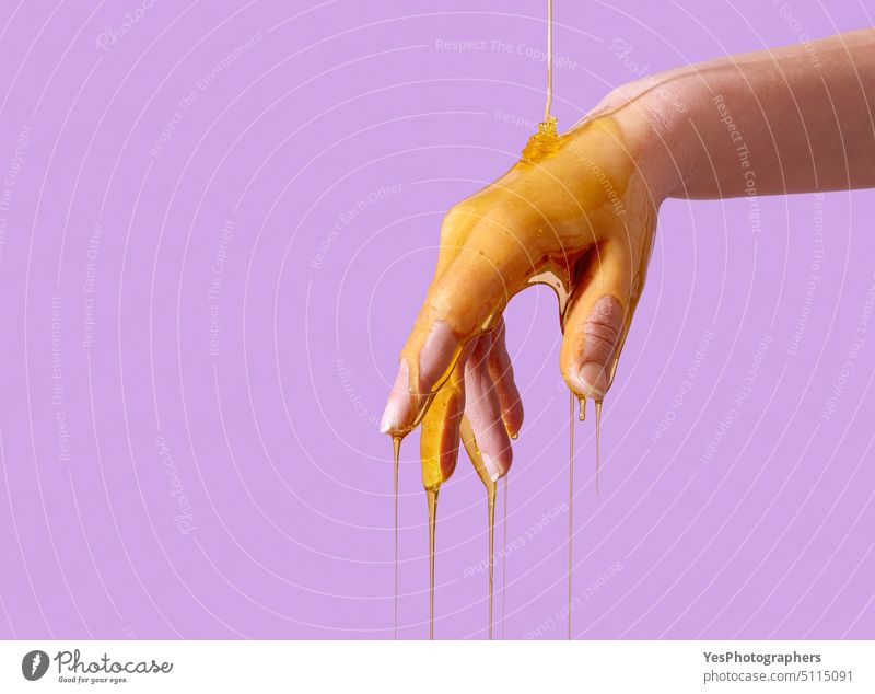 Hautpflege-Konzept, Gießen Honig über Hand, isoliert auf einem lila Hintergrund Alterung Antioxidans Arme Schönheit Biene Körper hell Pflege Nahaufnahme Farbe