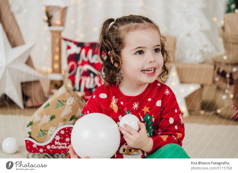 Lächelndes kleines Mädchen zu Hause mit Weihnachtskugeln in der Hand Kind Weihnachten heimwärts Geschenke Glück heiter niedlich 2 Kinder Familie Dezember