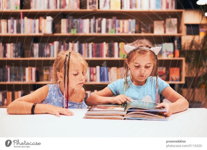 Zwei Grundschülerinnen machen Hausaufgaben in der Schulbibliothek. Schüler lernen aus Büchern. Schüler haben Spaß in der Bibliothek. Zurück zur Schule Rücken