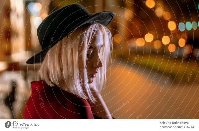 Porträt der jungen Frau mit blonder Frisur und Hut auf Nacht glühenden europäischen Stadt Hintergrund. Nasenpiercing. Person Großstadt Nachtleben Lifestyle