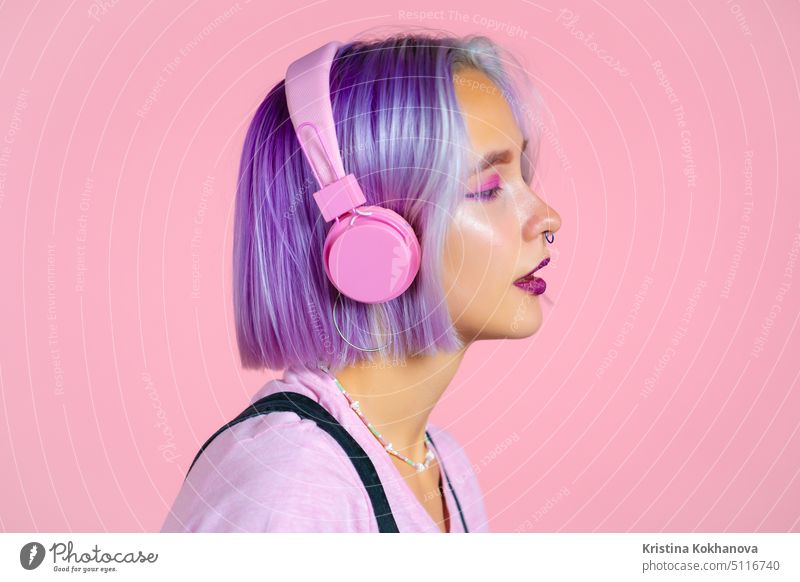 Close-up-Porträt von hübschen Mädchen mit gefärbten violetten Haaren hören Musik, lächelnd, tanzen in Kopfhörer im Studio gegen rosa Hintergrund. Musik, Tanz, Radio-Konzept