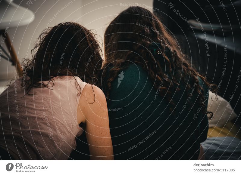 Zwei Freundinnen sitzen gemeinsam auf der Erde, mit dem Rücken gewandt zum Fotografen und besprechen etwas. Zusammensein dunkles Haar lässig Junge Frauen