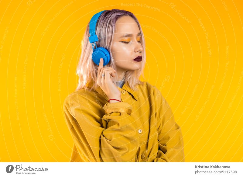 Schöne Frau mit rosa Haaren tanzen mit Kopfhörern auf gelben Studio Mädchen Teenager Gefühle ungewöhnlich trendy stylisch Schminke schön niedlich Person
