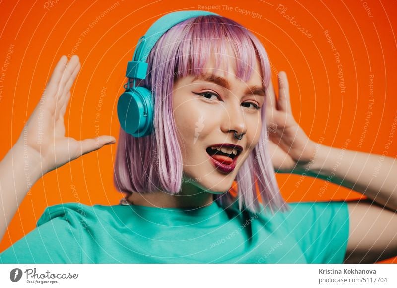 Außergewöhnliche Frau mit gefärbten violetten Haaren hört Musik mit Kopfhörern und singt auf orangefarbenem Hintergrund. Einzigartige Hipster Mädchen tanzen