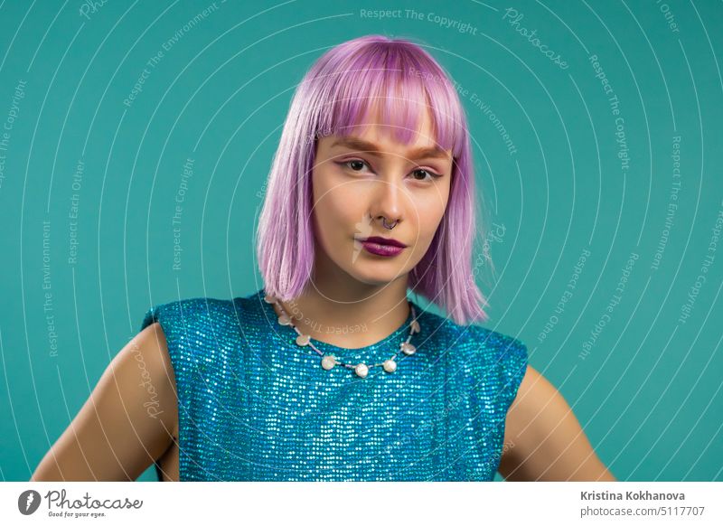 Porträt einer Hipster-Frau mit gefärbten violetten Haaren auf türkisfarbenem Studiohintergrund. Positives junges Partygirl schaut in die Kamera. Erstaunlich funkelnden Outfit