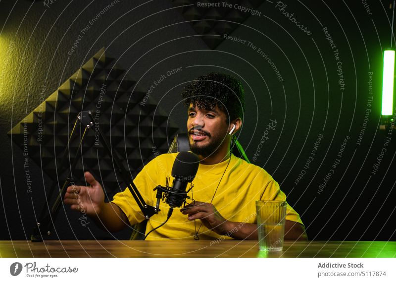Hispanischer Podcast-Moderator erzählt Geschichte Mann Wirt Aufzeichnen Lächeln teilen Etage dunkel Mikrofon neonfarbig männlich jung hispanisch ethnisch