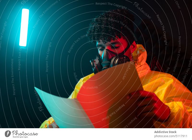 Hispanischer Chemiker liest Akte im dunklen Labor Mann lesen Aktenordner ungesetzlich dunkel Nacht neonfarbig leuchten männlich jung hispanisch ethnisch