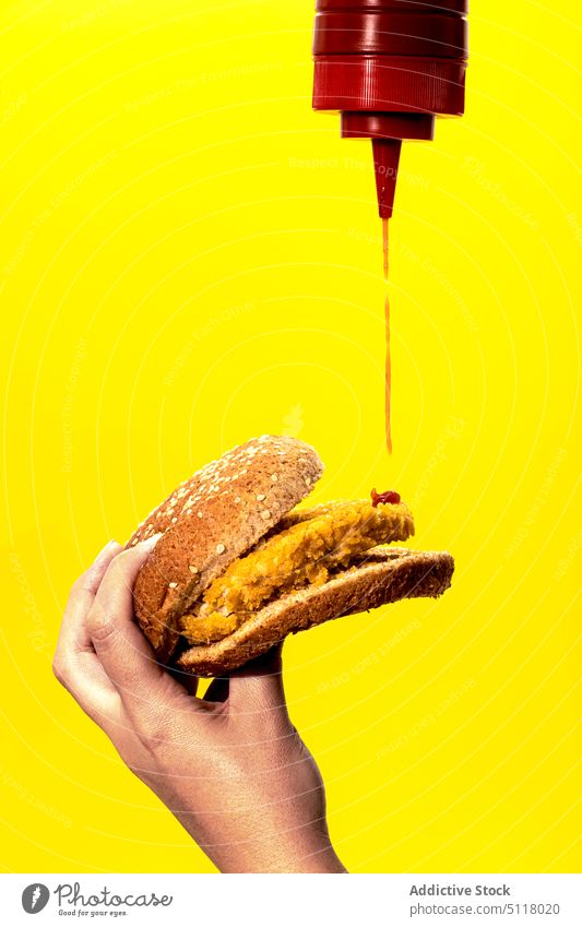 Crop Frau gießt Tomatensauce auf Burger in gelbem Studio Ketchup Fastfood ungesund selbstgemacht eingießen Junk Food hungrig Lebensmittel geschmackvoll