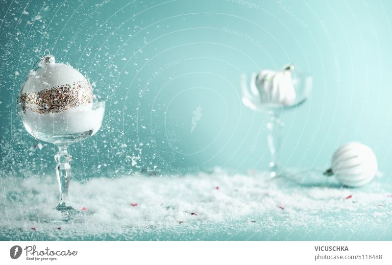 Champagnergläser gefüllt mit Schnee und weißen Weihnachtskugeln auf blauem Hintergrund mit fallendem Schnee weihnachtskugeln fallender Schnee verschneite Glas