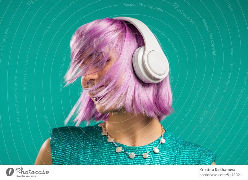 Ungewöhnliche trendige Frau mit gefärbten violetten Haaren hört Musik, tanzt mit Kopfhörern auf türkisem Hintergrund. Fashionista Teenager-Mädchen Person Spaß
