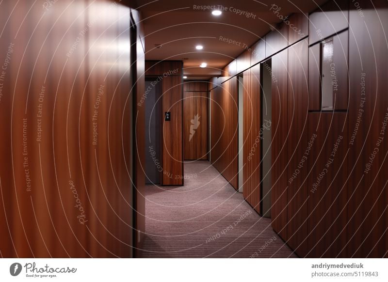 Leerer, dunkler Innenraum des modernen Hotelkorridors mit holzgetäfelten Wänden, eleganten Teppichen und Beleuchtung an der Decke. Gang Tür Innenbereich Holz
